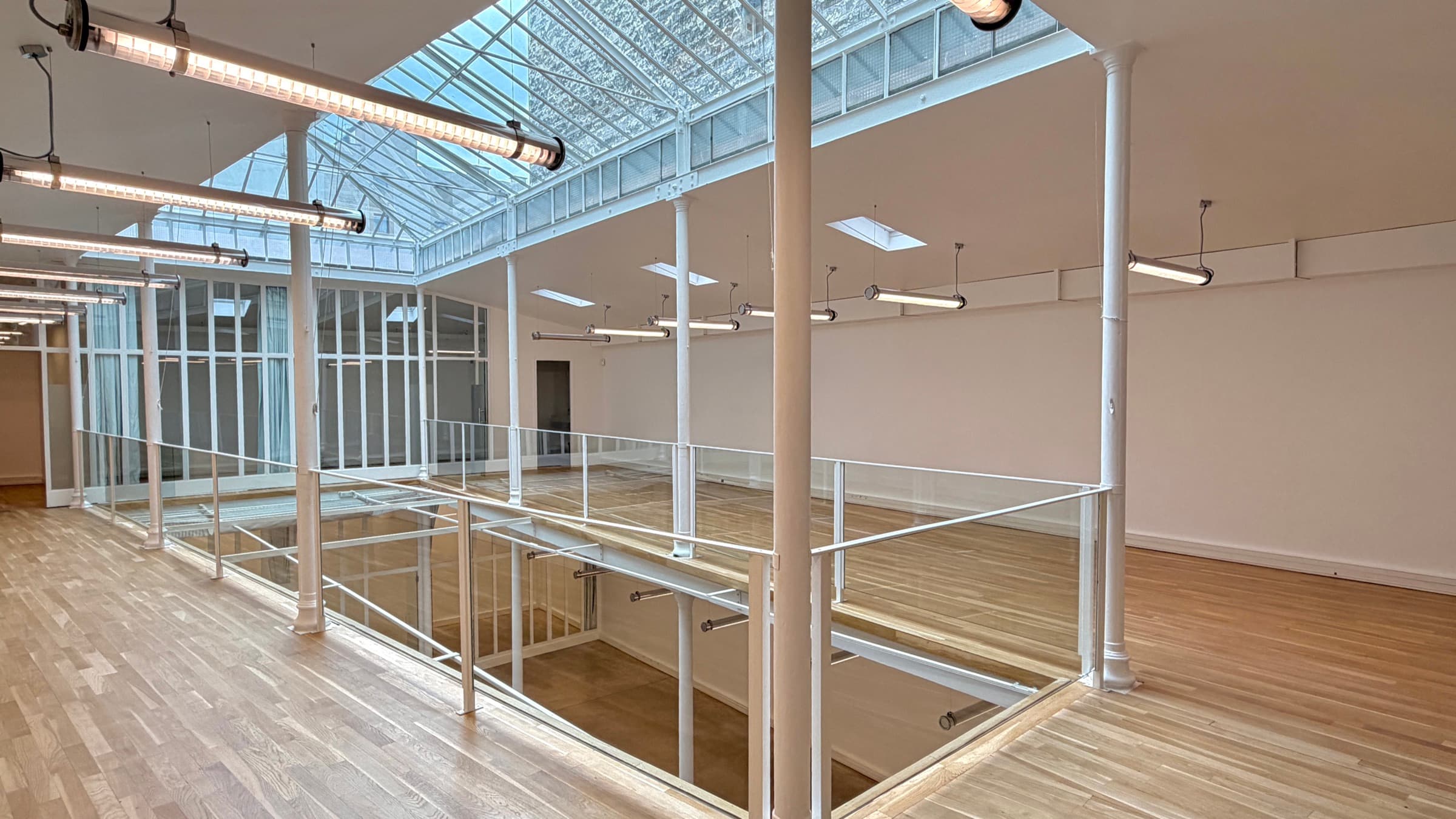 Mezzanine avec colonnes en fonte blanches, garde-corps en verre et luminaires tubes allumés