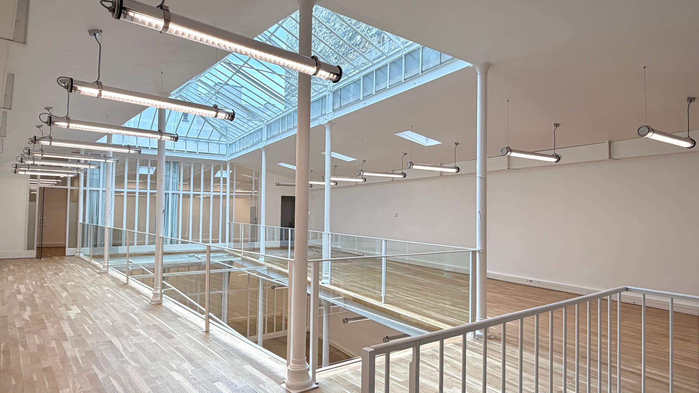 Mezzanine au parquet chêne avec cascade de luminaires suspendus sous la verrière zénithale