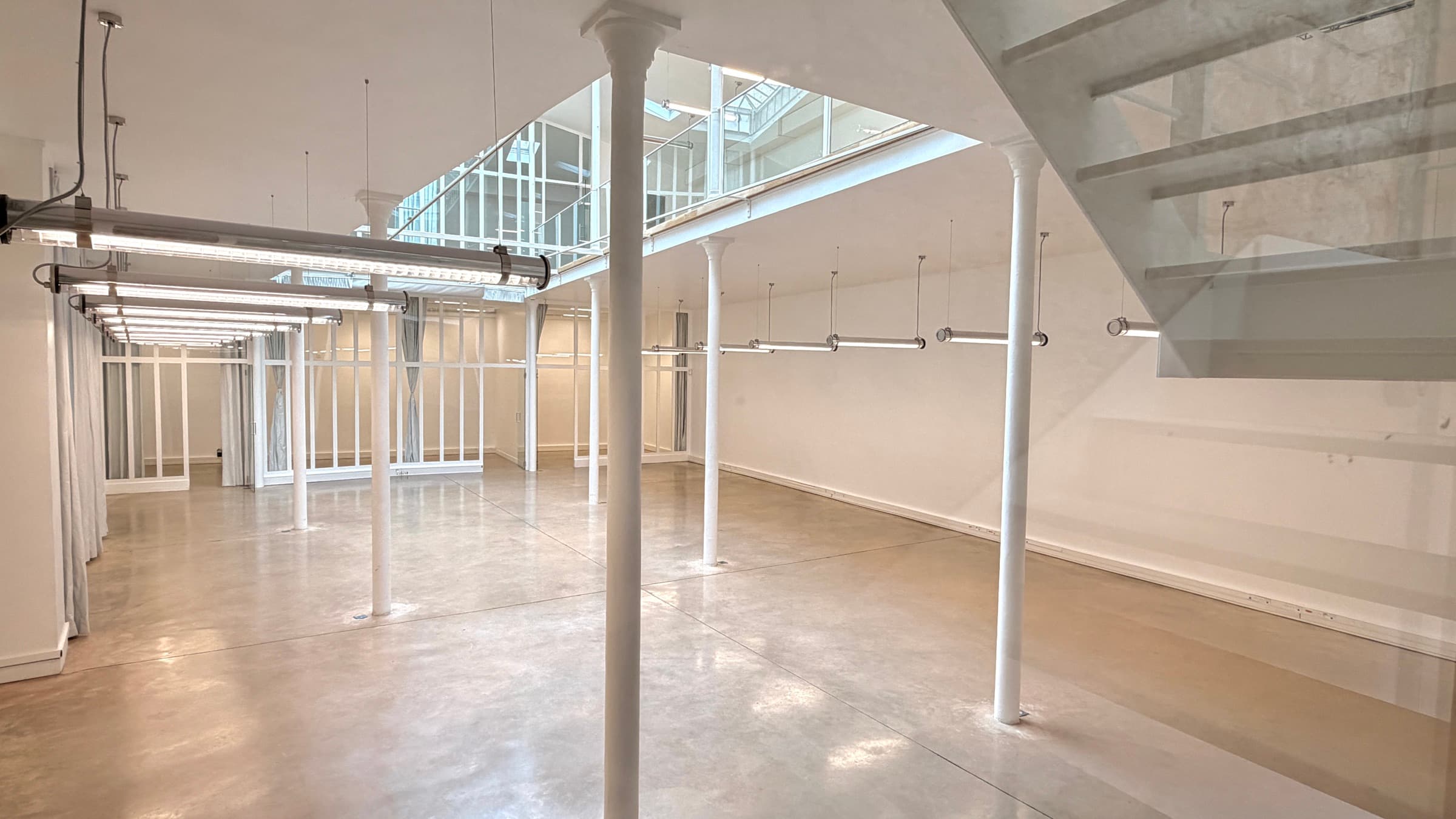Plateau RDC en béton ciré avec colonnes fines et cloisons verrières au fond