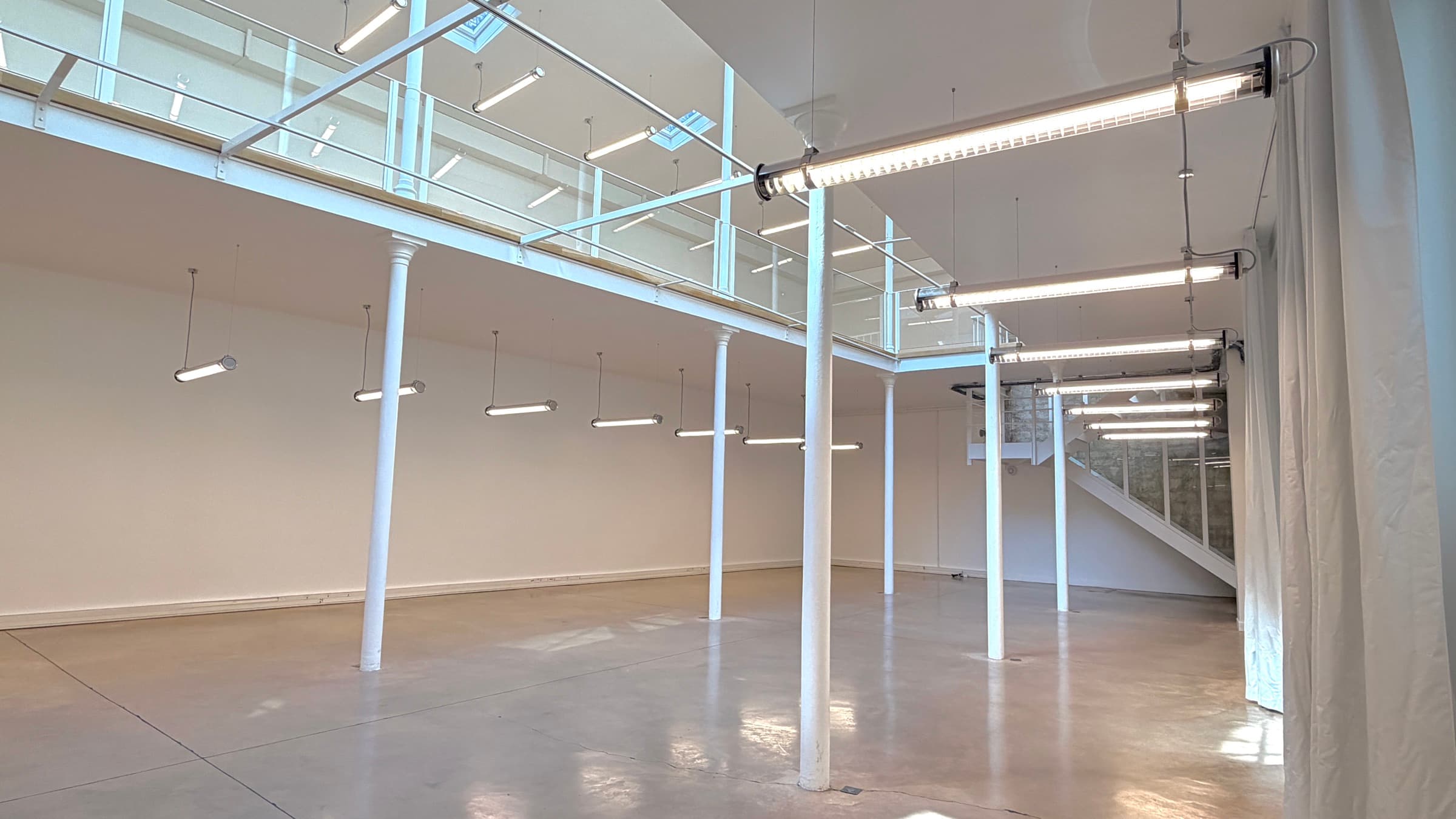 Plateau du RDC sous la mezzanine, double hauteur, colonnes et néons alignés