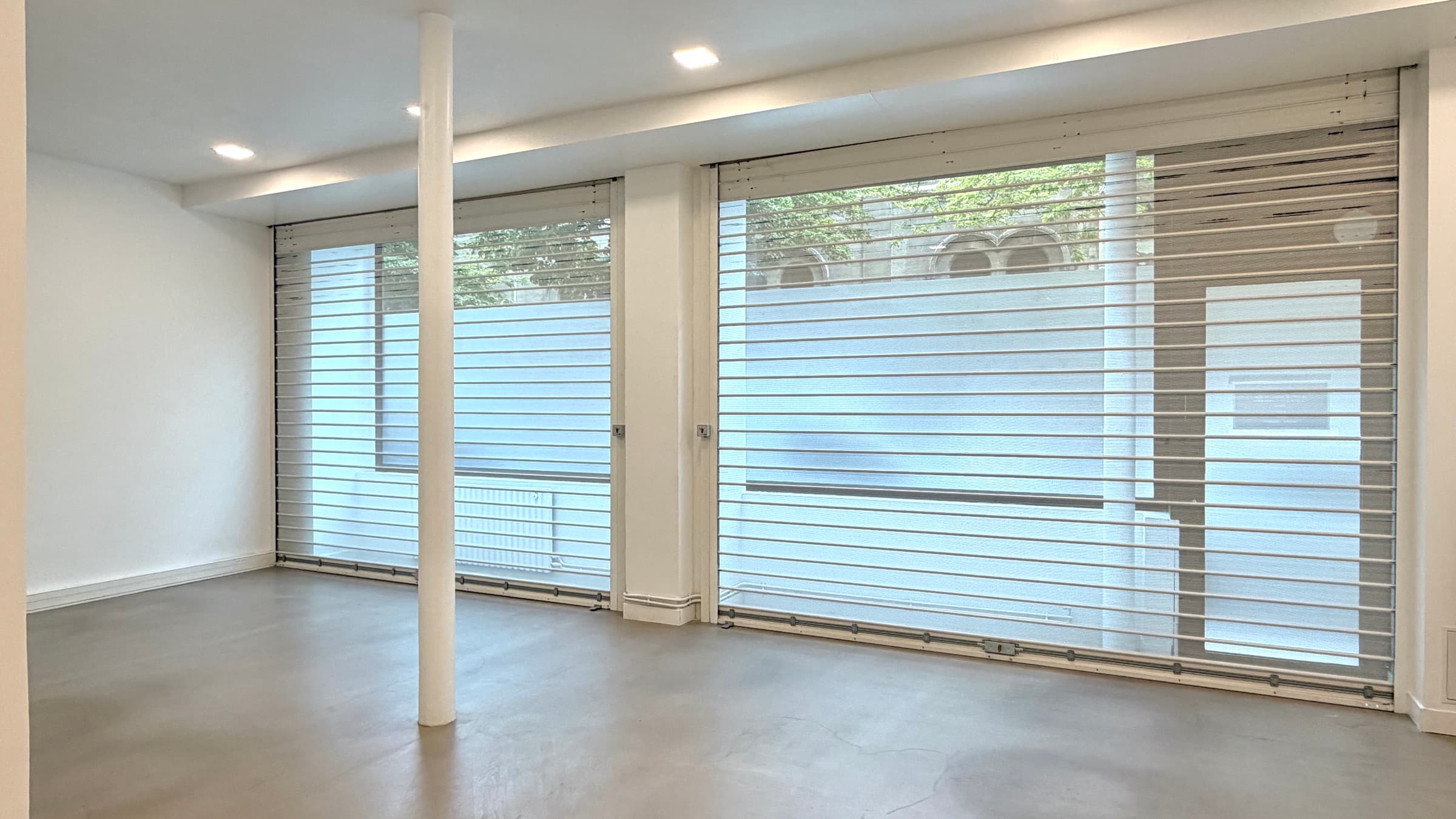 Salle vitrine sur rue en béton ciré avec deux grandes baies et rideaux métalliques ajourés