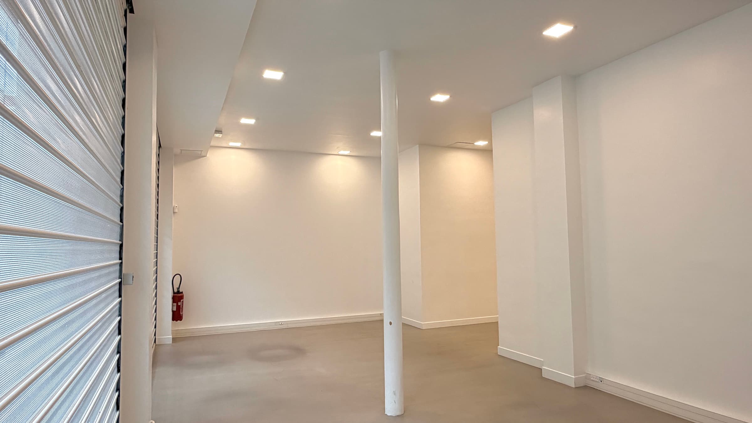 Salle vitrine côté rue avec rideau de fer perforé filtrant la lumière