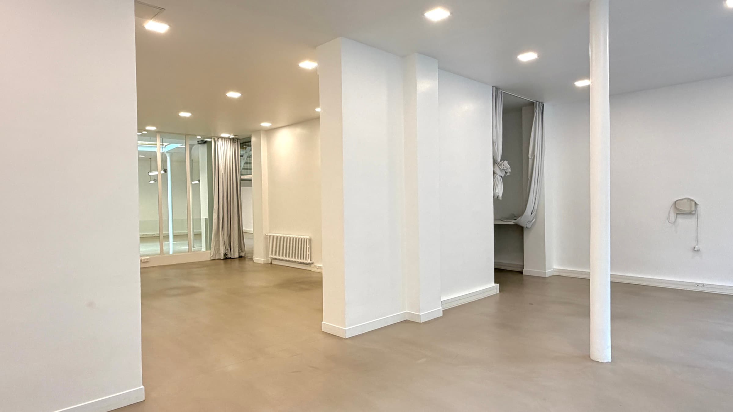 Volume blanc de la salle vitrine avec spots, piliers et vitrage sur le plateau
